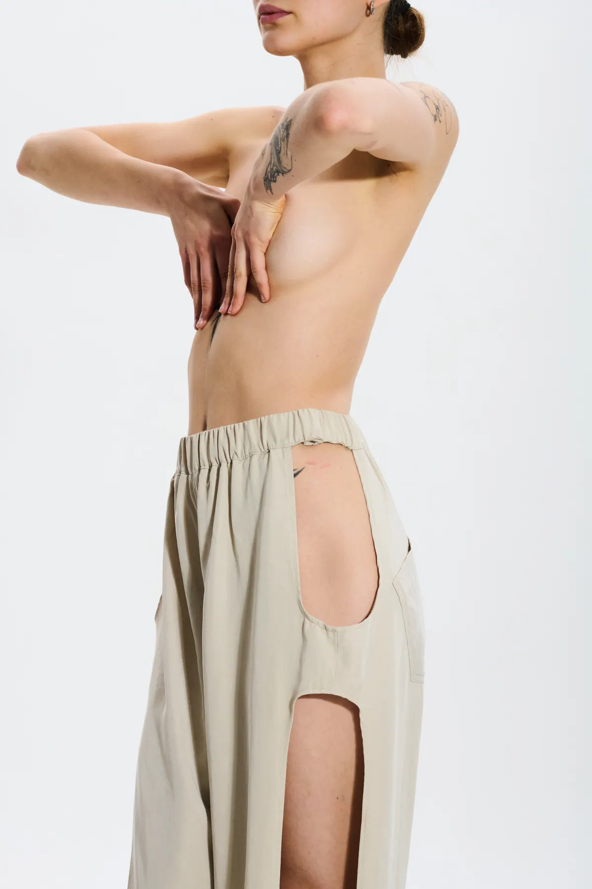 A bare back, arm drawn across the shoulder, above cream tailored trousers