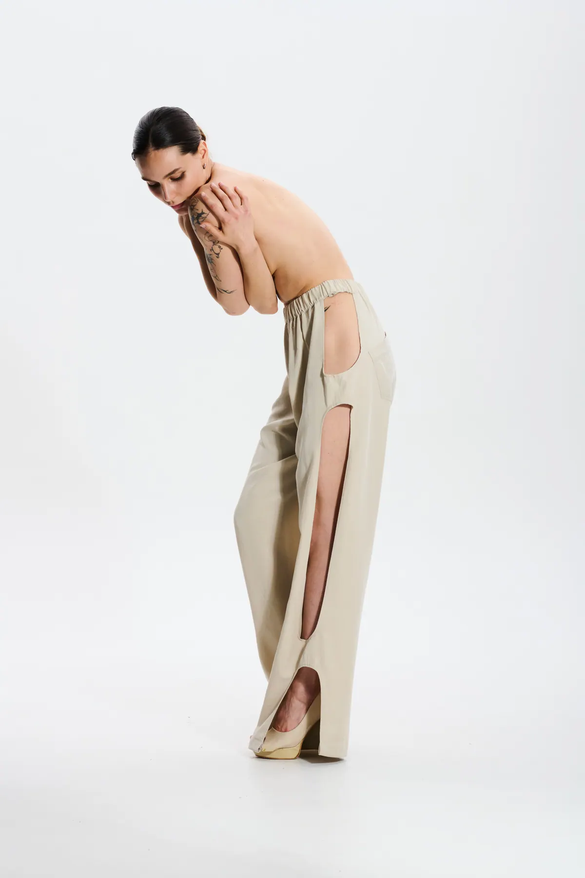 A model leans forward in cream trousers with open side seams, back bare