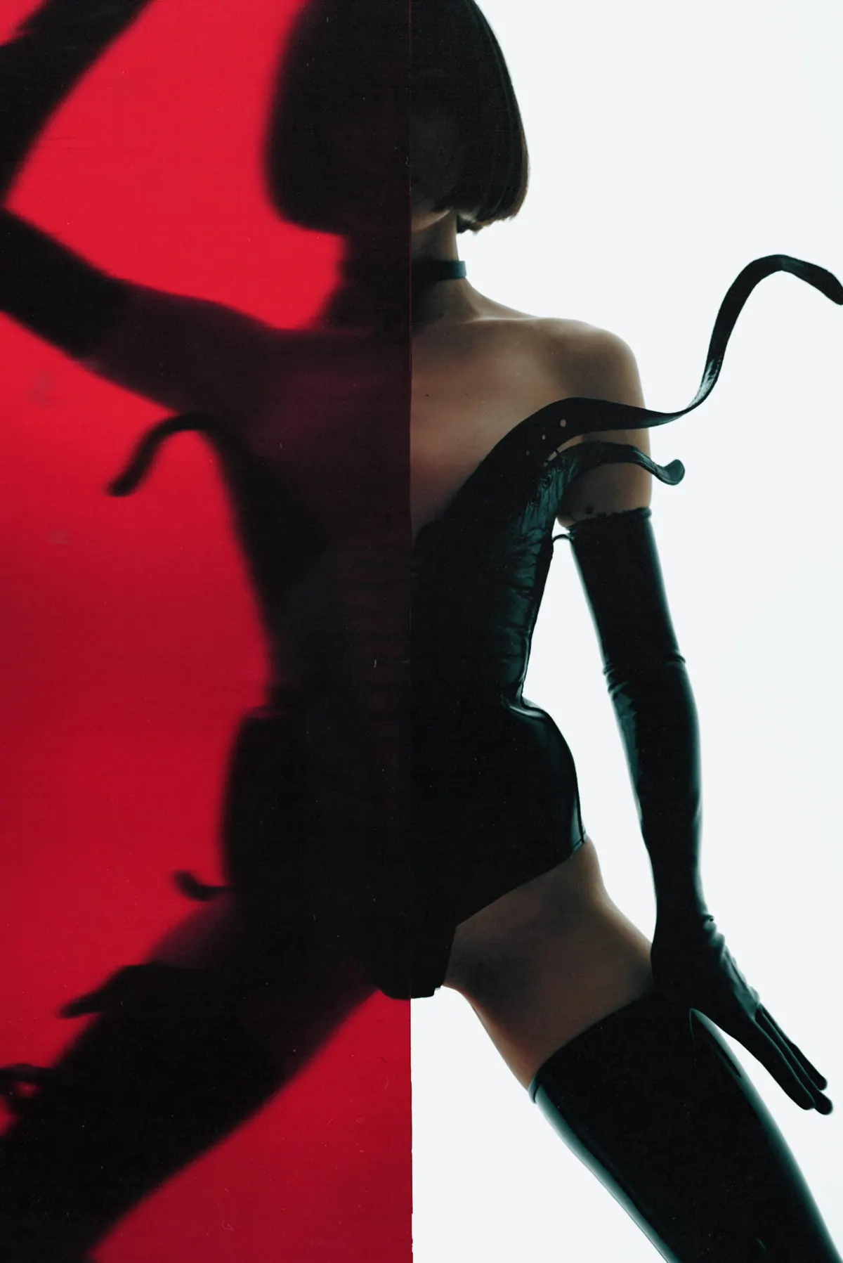 Shadow hands cast across a red panel beside a model in leather gloves and boots